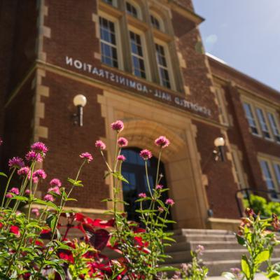 Pink flowers in front of Schofield Hall on a sunny day.