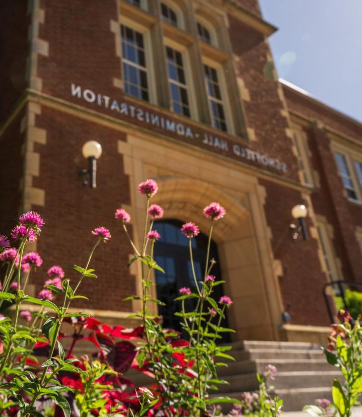 Pink flowers in front of Schofield Hall on a sunny day.